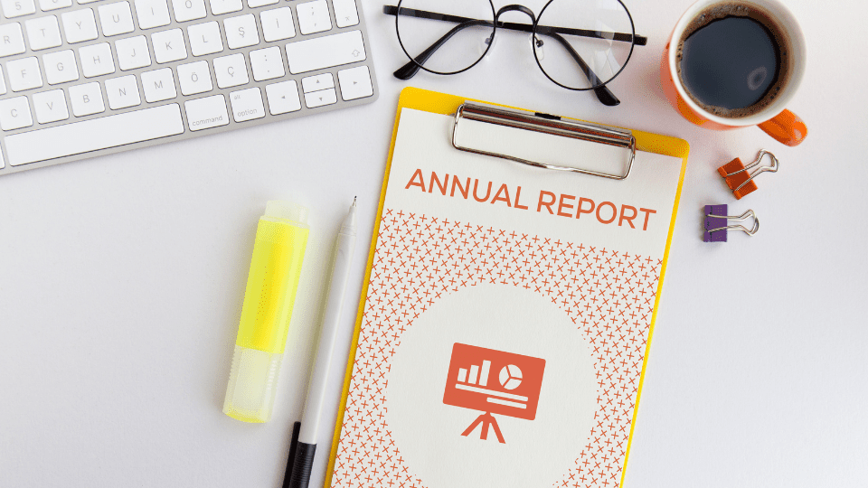 An annual report on a clipboard next to a keyboard, a pair of glasses, a highlighter, and a cup of coffee
