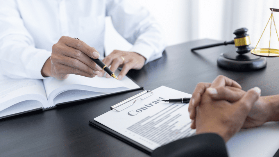 Two people sitting at a table with a legal document and pens to sign it.