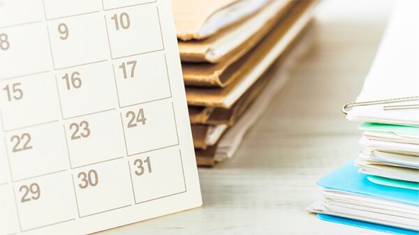 A calendar on desk next to stack of papers