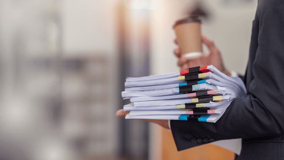 A person in a suit holding a stack of papers and a cup of coffee