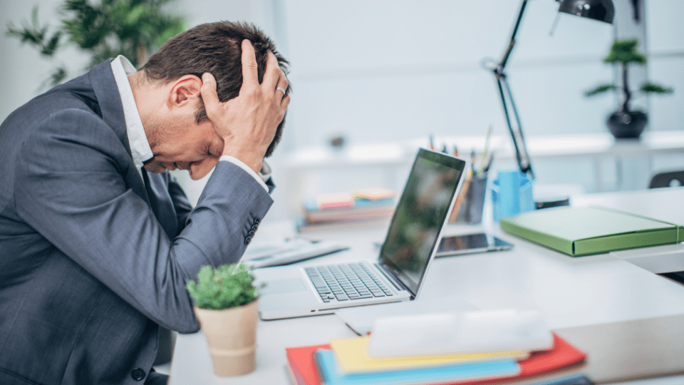 A person in a suit is sitting at their desk with their head in their hands.