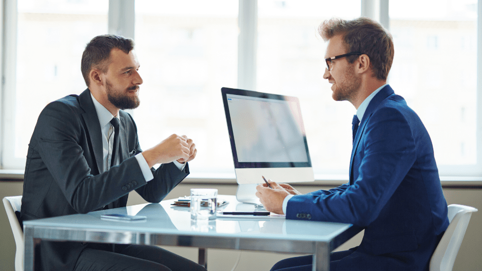 Two people in suits sitting at a table in an office.