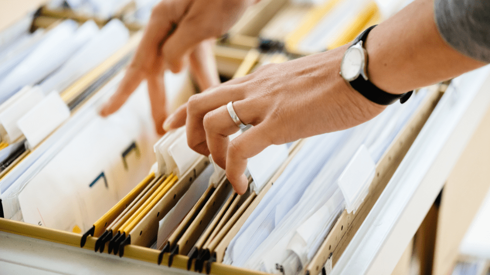 A person's hand is reaching into a file drawer.