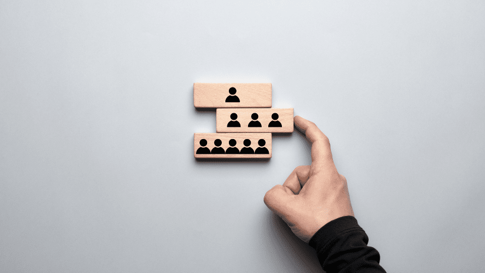 A person’s hand pushing a block with three figures, while other blocks with one and five figures represent different stages of business structure growth