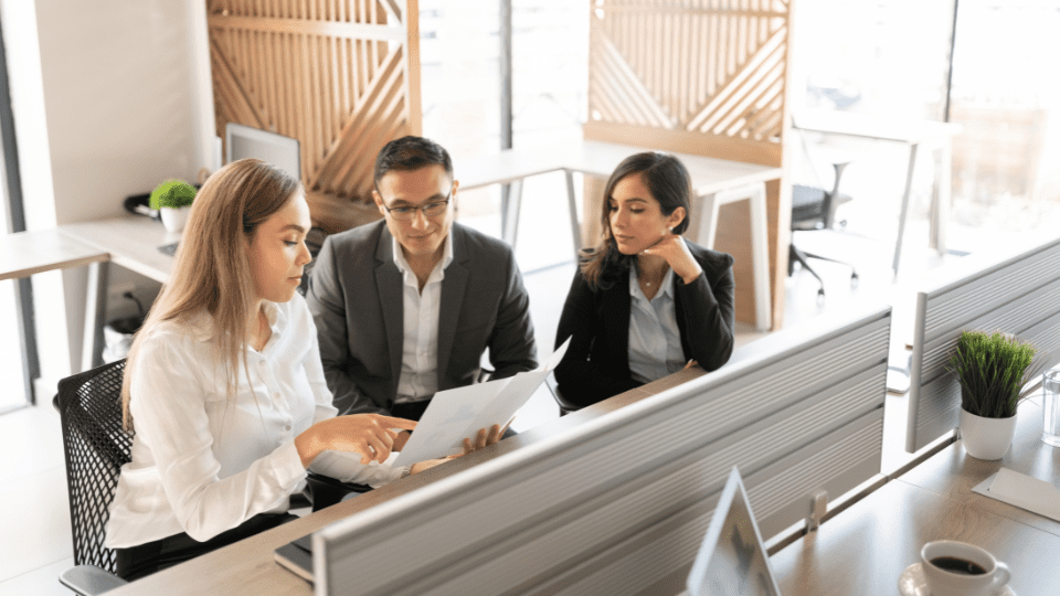 Three people sitting at a desk in an office carefully reviewing an SOI before submitting it
