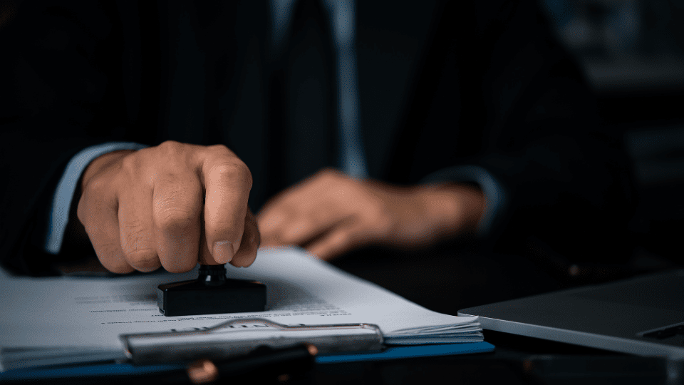 A person in a suit in authority is using a rubber stamp to put a stamp on a piece of paper