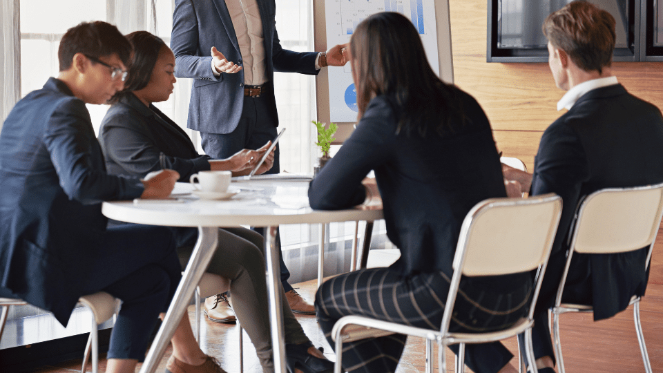 A group of people sitting around a table in an office while one person gives a presentation