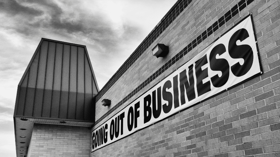 A black and white photo of a building with a sign that says “Going Out of Business”