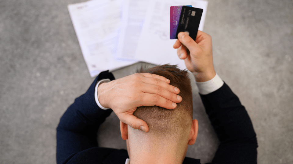 A person in a suit holding credit cards putting their head down in despair.