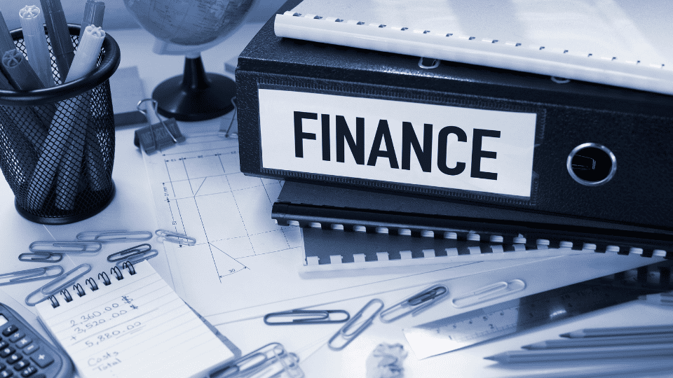 A binder with “Finance” written on it surrounded by paper, pens, a calculator, and a notepad.